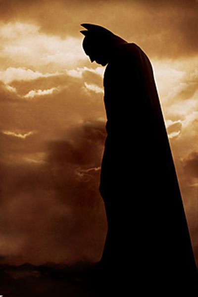 Batman stands moodily in a cloudy dark brown sky.